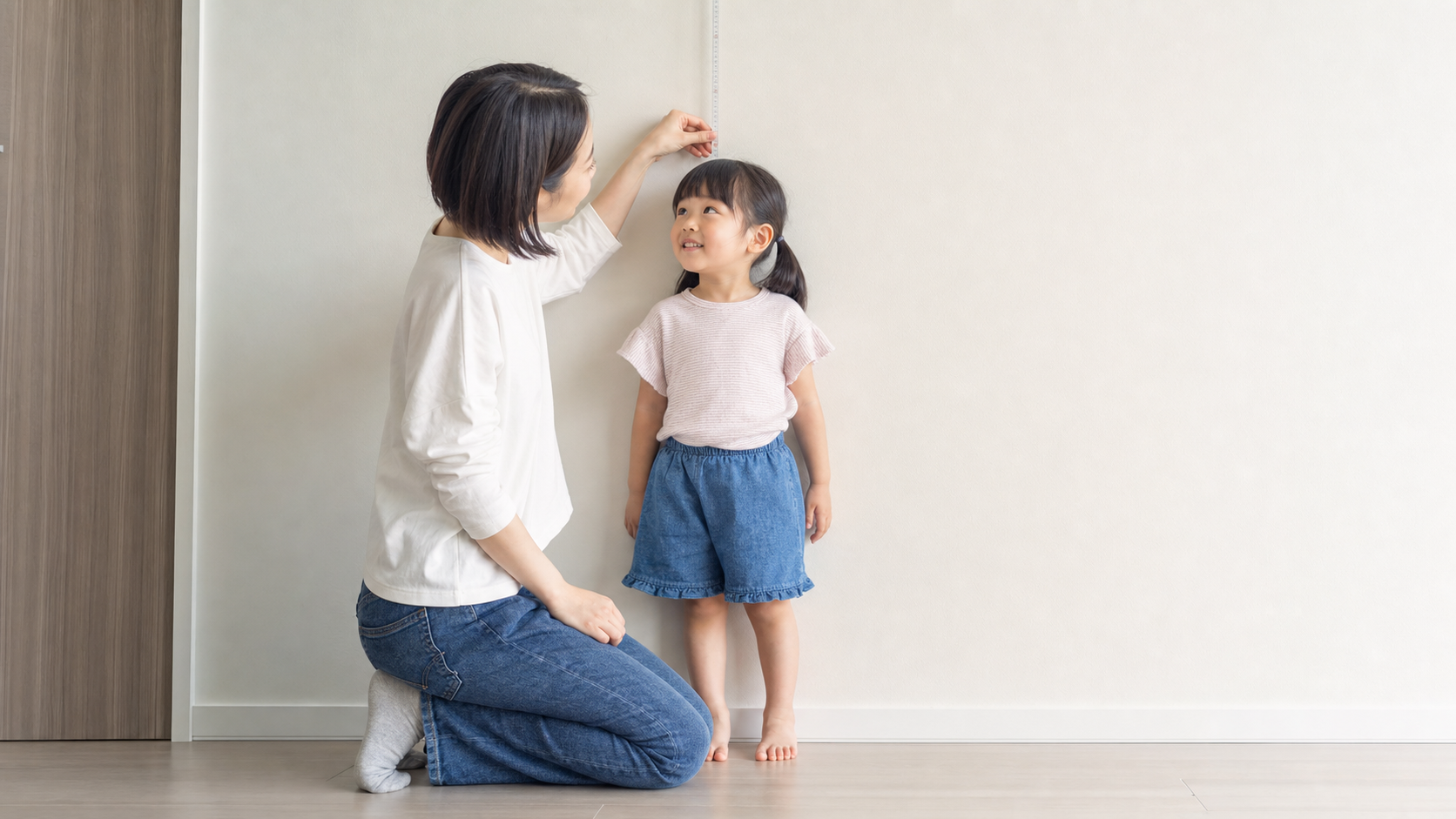 Parent measuring a young child's height against a plain wall